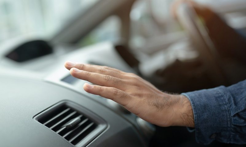 Close-up of male driver’s hand checking the air conditioning in a car.