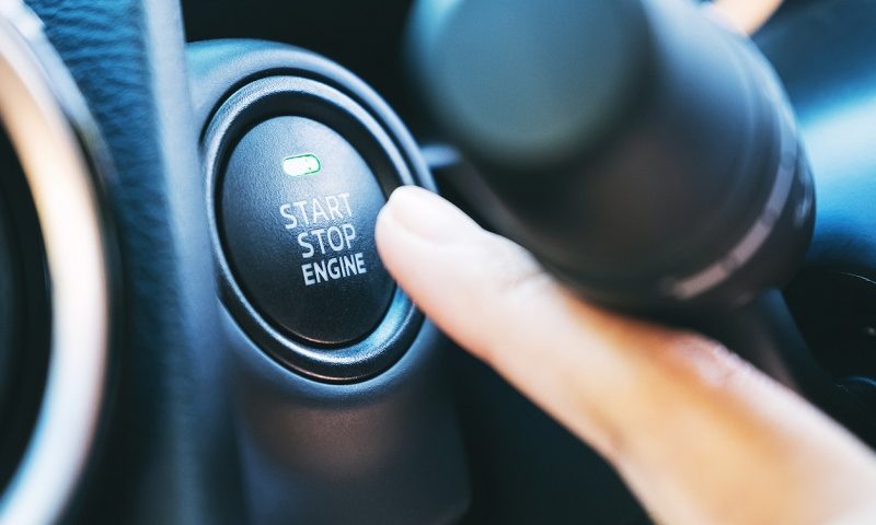 Someone pushing the start engine button on a car dashboard