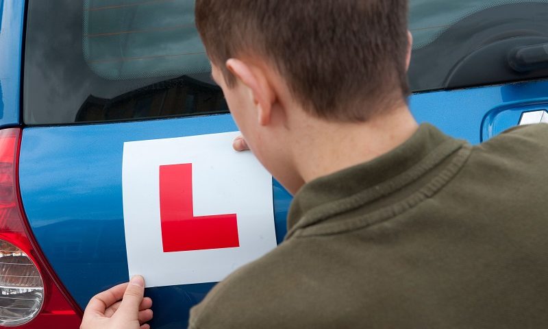 A young person putting an L plate on their blue car