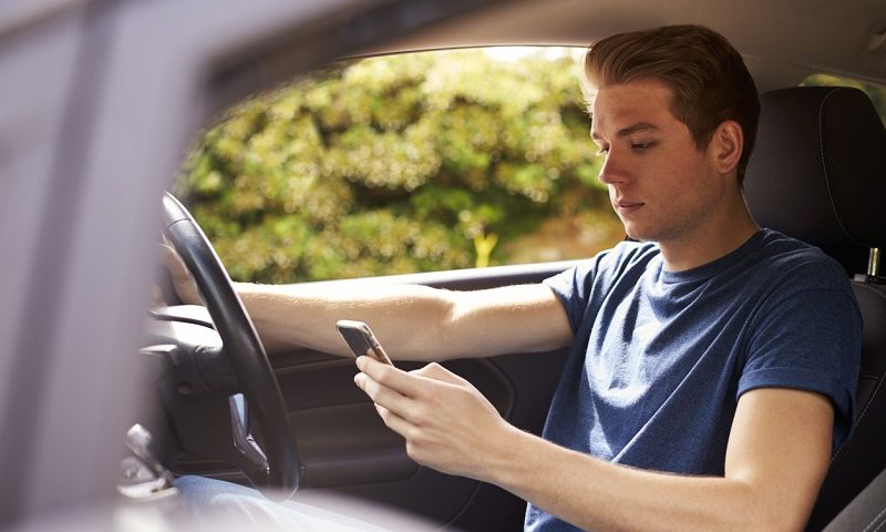 A young man uses a mobile phone while driving.