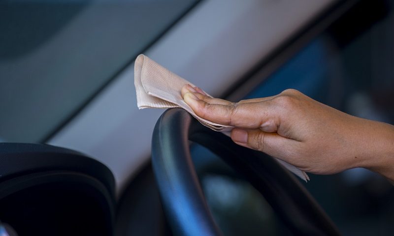 Person cleaning the car steering wheel with napkin