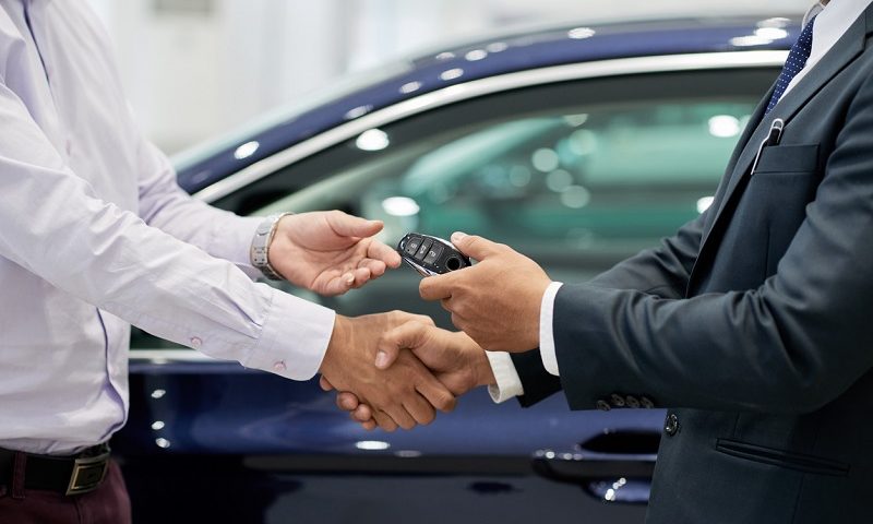 Salesman giving car keys to customer and shaking his hand