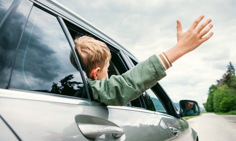 Young boy waving his hand outside a car window