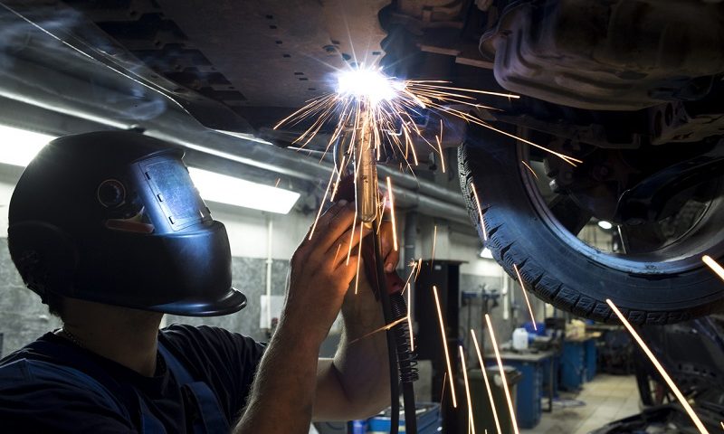 Mechanic wearing protective mask fixing the underside of a car