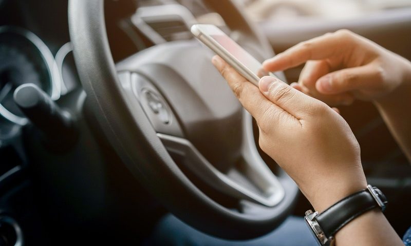 Person holding a mobile phone in their hand while driving