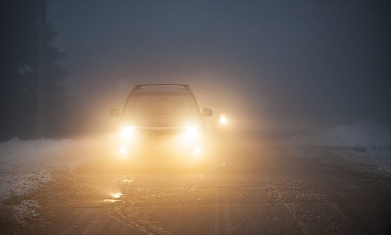 Bright headlights of a car driving on foggy winter road