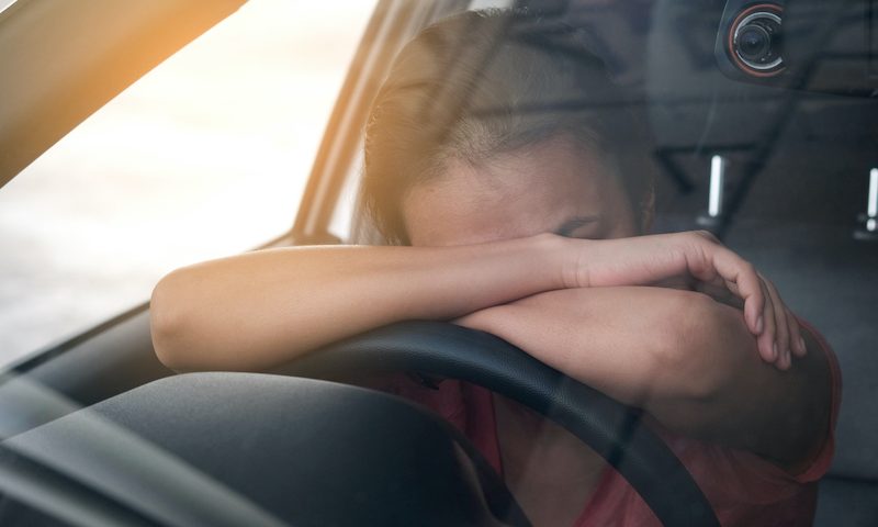 Sleepy woman resting her arms and head on the steering wheel.