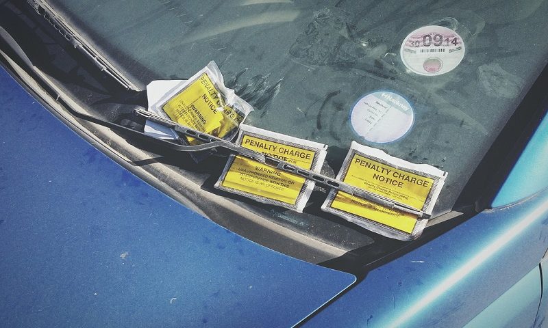 Close up of three parking tickets on the windscreen of a blue car.