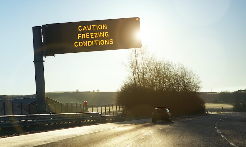 Vehicle passing road sign cautioning freezing conditions