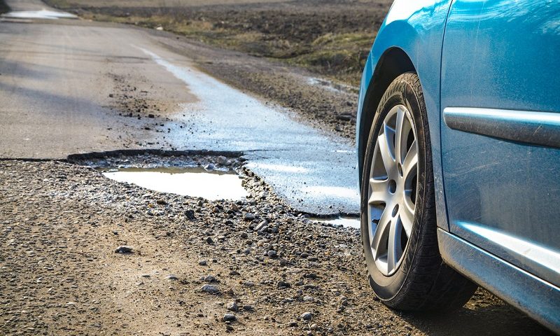 Car next to a pothole on an open road